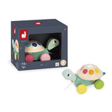 Janod Juratoys Pull Along Turtle, a wooden toy with a colorful spotted shell and rolling wheels, shown inside and outside its box.