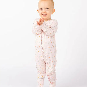 A baby stands clapping in Emerson and Friends’ Sleeper, Sweet Blooms bamboo pajamas, smiling against a plain white background.