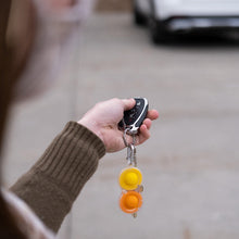 Load image into Gallery viewer, Person with car key and a clear Simpl Dimpl keychain from Fat Brain Toy Co, pointing at a parked car.
