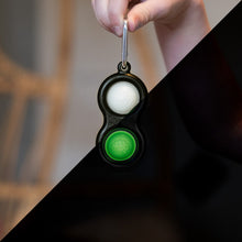 Load image into Gallery viewer, A hand with a Fat Brain Toy Co Simpl Dimpl Glow-in-the-Dark adds magic and tactile fun to your essentials.
