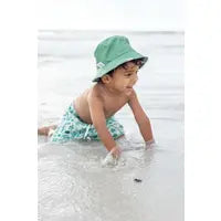 Load image into Gallery viewer, A baby in an Emerson and Friends Sea Turtles Reversible Bucket Hat plays happily in the sand by the beach.

