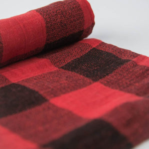 A rolled-up Cotton Swaddle in Red Plaid by Little Unicorn lies on a white background.